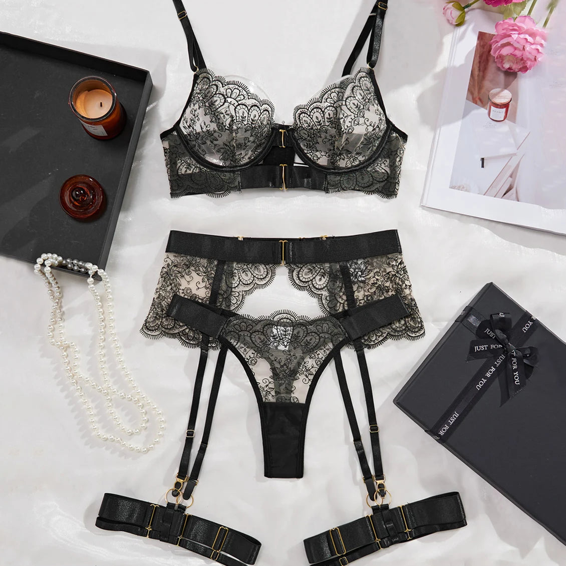 Black lace lingerie set with garters on a light surface with decorative items.